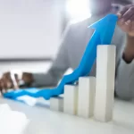 Mão segurando seta azul ascendente sobre gráfico de barras, representando crescimento de vendas com inteligência artificial