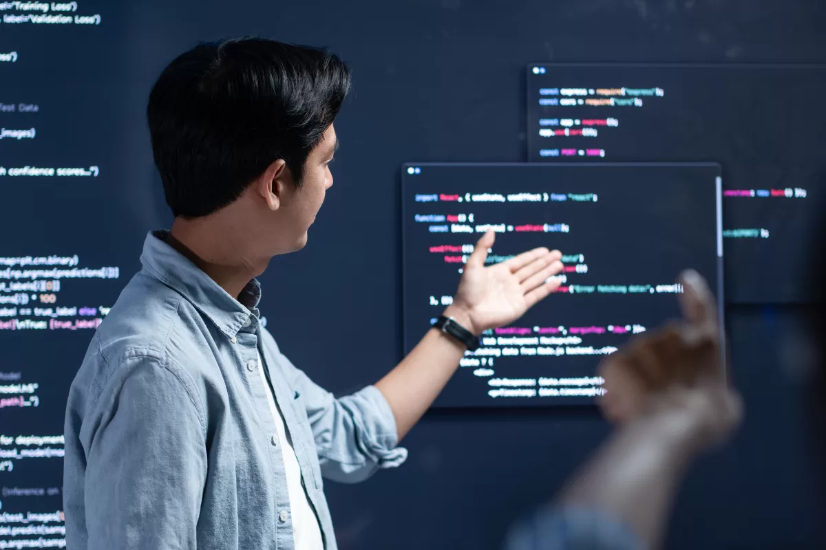 Developer presenting code on a large screen to a colleague during the software discovery phase, a technical alignment step before development begins