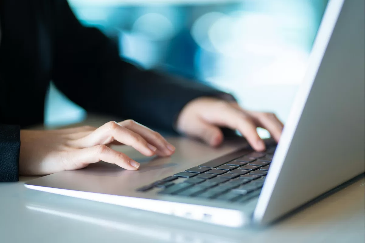 Person typing on a laptop in a work environment, representing the management and monitoring of outsourced software projects