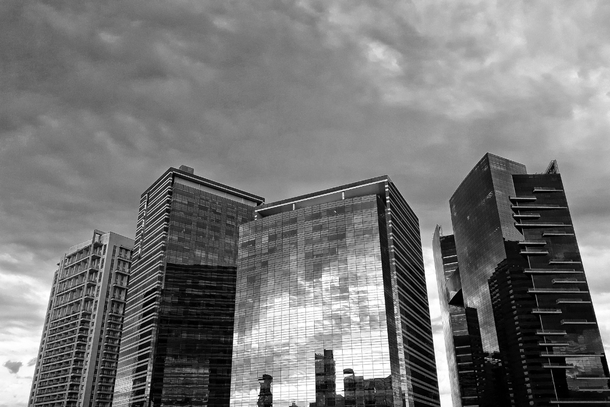 Conjunto de edifícios comerciais modernos com fachada de vidro refletindo o céu nublado, em fotografia preto e branco