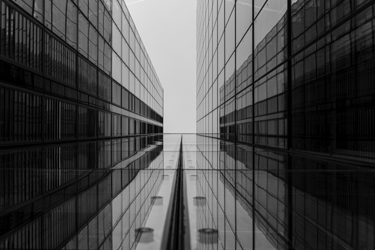 Corredor simétrico entre dois edifícios espelhados de vidro fotografado de baixo para cima, representando precisão e inovação em desenvolvimento de software
