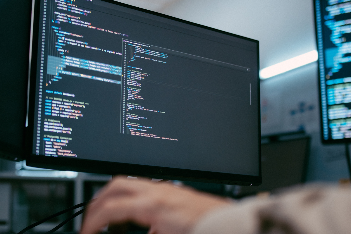 Technology professional working in front of monitors displaying code, representing a software development outsourcing team