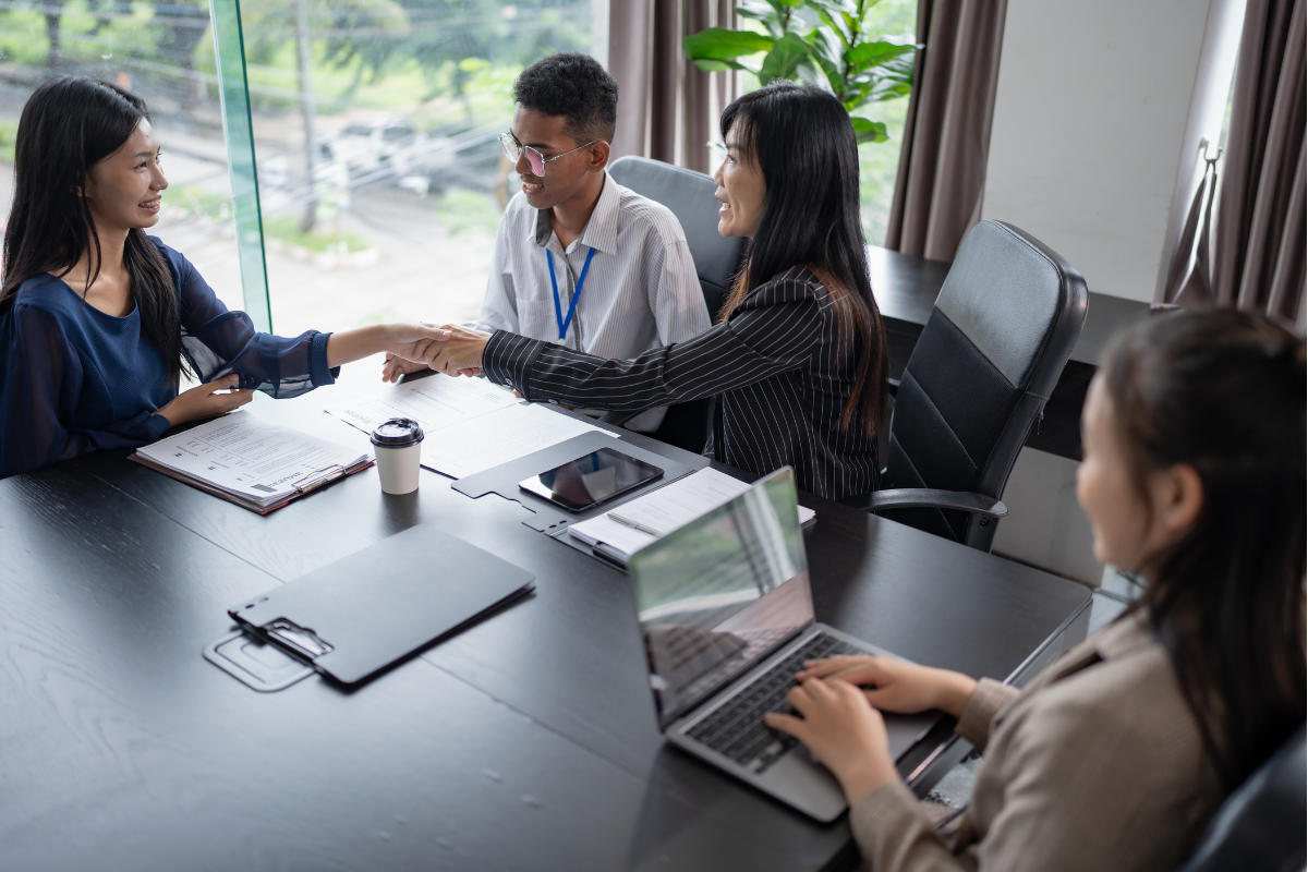 Profissionais em reunião de negócios com aperto de mãos sobre a mesa, representando processo de recrutamento e seleção com apoio de inteligência artificial