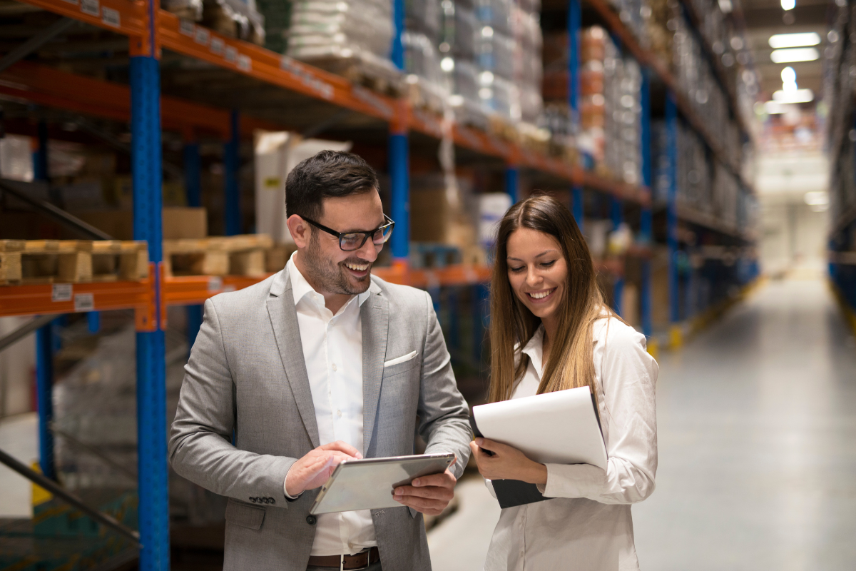 Two managers reviewing inventory management software on a tablet inside a warehouse