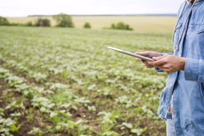 Produtora rural segurando tablet em campo agrícola, usando tecnologia e dados para gestão no agronegócio