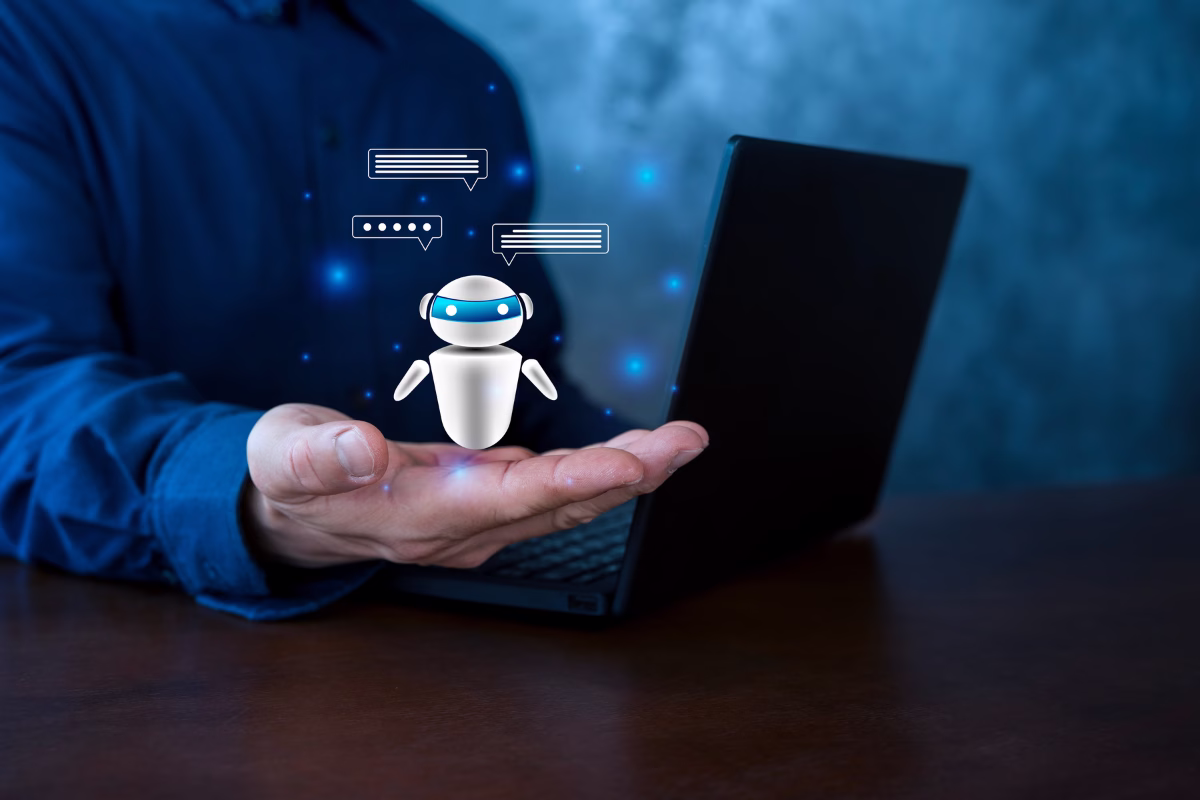 A man in a blue shirt holding an open laptop with a small futuristic robot floating above his open palm. The robot displays digital chat bubbles and blue neon light dots in the background, symbolizing virtual customer service and artificial intelligence.