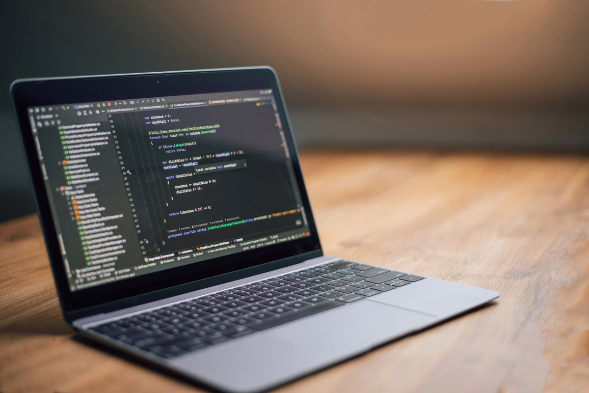 Open laptop on a wooden desk displaying lines of programming code on a dark screen of a development editor (IDE).