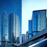 Fachada de arranha-céus com vidro azul refletindo outros edifícios em centro comercial representando 10 melhores fábricas de software no Paraná.