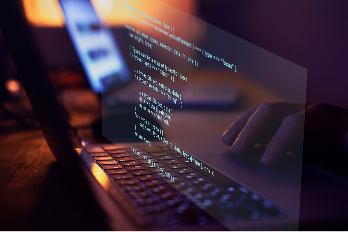 Developer's hand typing on a laptop with source code projected in blue and orange tones, representing the software development process