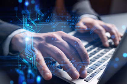 Empresário digitando em um notebook, com um holograma de circuito eletrônico azul sobreposto às mãos, simbolizando tecnologia e transformação digital.