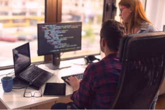 Desenvolvedor e colega revisando código TypeScript em monitor de escritório