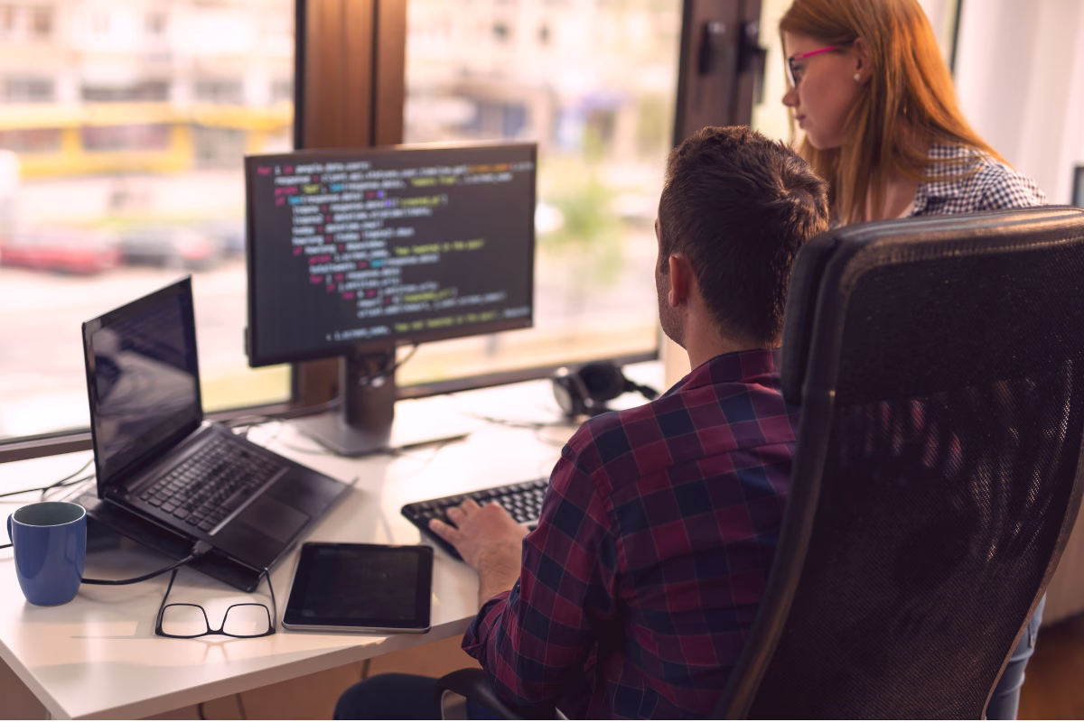 Desenvolvedor e colega revisando código TypeScript em monitor de escritório