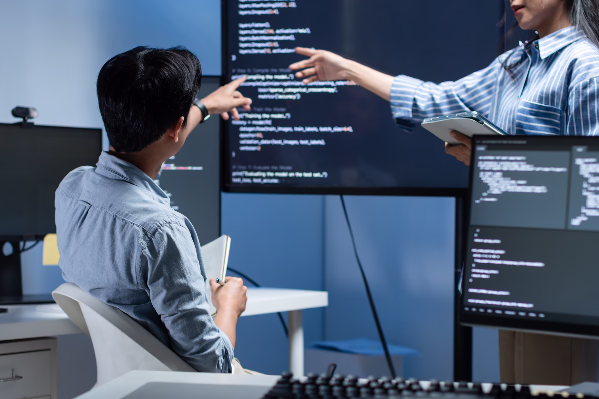 Technology professionals reviewing AI model code on monitors during a software development team meeting