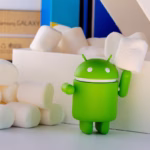 Boneco verde do mascote do Android segurando um marshmallow, ao lado de uma pilha de marshmallows e de uma caixa branca.