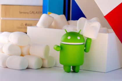 Boneco verde do mascote do Android segurando um marshmallow, ao lado de uma pilha de marshmallows e de uma caixa branca.