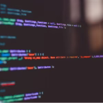 Tela de computador desfocada exibindo linhas de código com o logo do TypeScript (TS) em destaque no canto inferior direito.