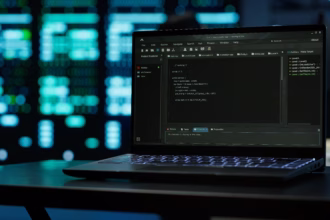 Notebook aberto sobre uma mesa exibindo código em um ambiente de desenvolvimento, com servidores de um data center iluminados ao fundo.