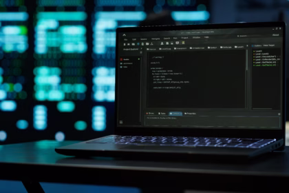 Notebook aberto sobre uma mesa exibindo código em um ambiente de desenvolvimento, com servidores de um data center iluminados ao fundo.