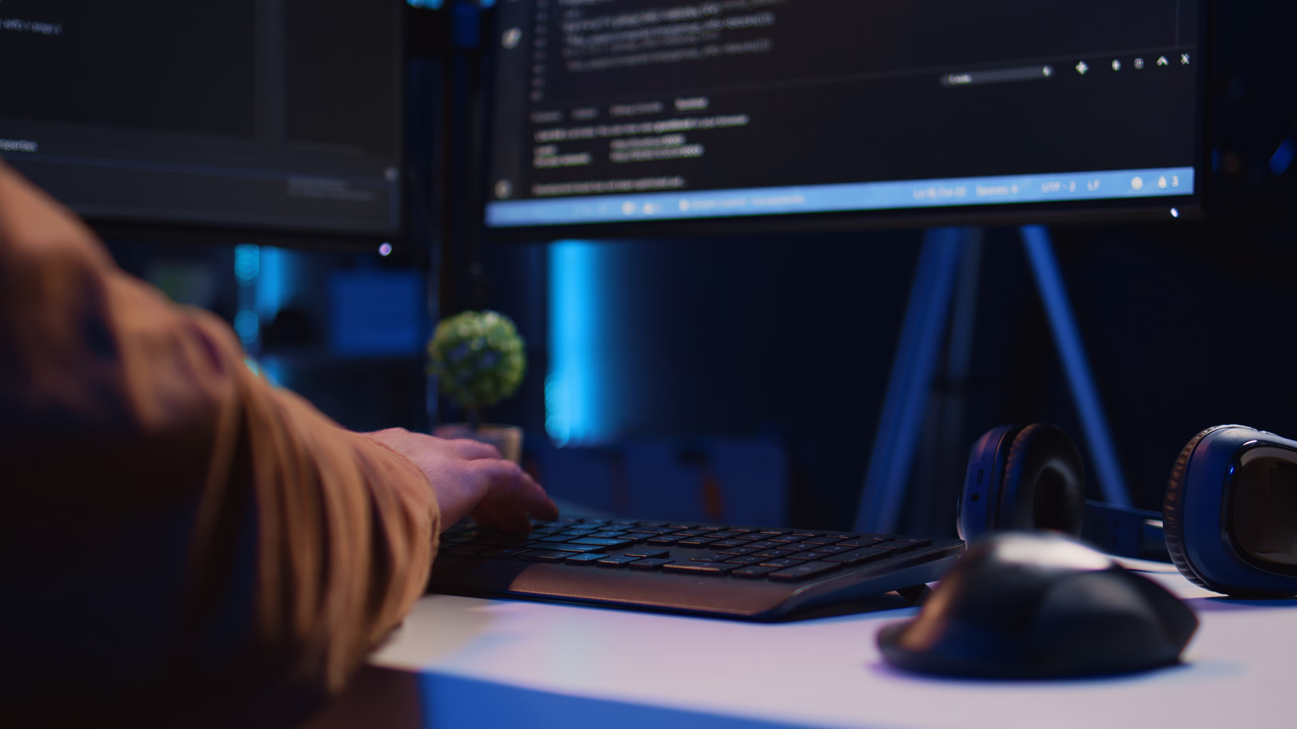 Desenvolvedor digitando em um teclado em frente a monitores com código-fonte, em um ambiente de trabalho com iluminação azul