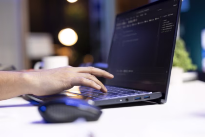 Mão de uma pessoa digitando em um notebook com código exibido na tela, representando o trabalho de desenvolvimento de software.