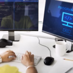 Desenvolvedor programando em uma estação de trabalho com dois monitores, um exibindo linhas de código e outro com a palavra "Programming"