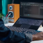 Desenvolvedor programando em laptop em ambiente de trabalho remoto, com editor de código aberto na tela.