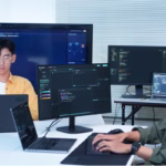 Desenvolvedores de uma fábrica de software trabalhando com notebooks e monitores exibindo código em um escritório de tecnologia