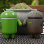 Dois bonecos do robô Android, um verde e um cinza com detalhes metálicos, lado a lado sobre uma mesa, representando o desenvolvimento Android com Kotlin.