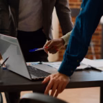 Equipe reunida em volta de um notebook, analisando relatórios e gráficos sobre a mesa.