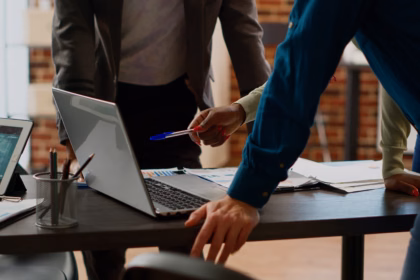Equipe reunida em volta de um notebook, analisando relatórios e gráficos sobre a mesa.