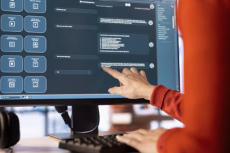 Pessoa de suéter vermelho aponta para a tela de um monitor que exibe uma interface de assistente de IA, com um chat de perguntas e respostas e atalhos para criar vídeo, imagem, calendário e texto.